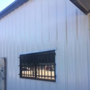 White building wall with a barred window and dark roof edge in sunlight