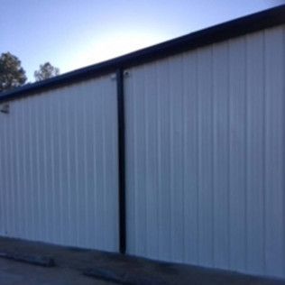 White metal-sided building with a dark roof and vertical support beam, seen from the side.