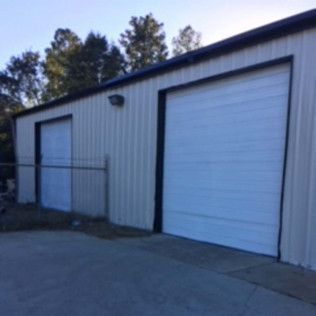 Small industrial building with a white roll-up garage door and a fenced side entrance.