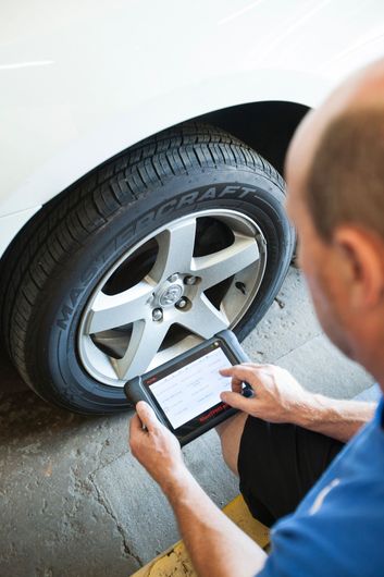Mechanic inspecting a car tire with a tablet beside a white vehicle
