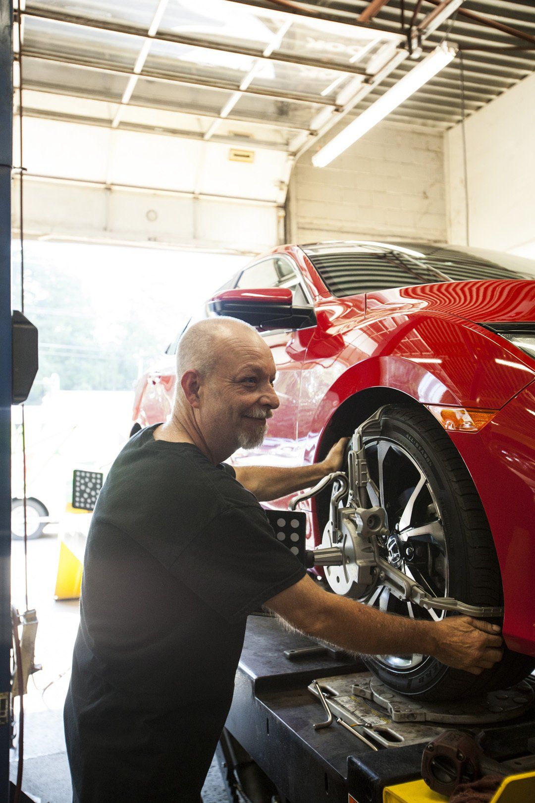 Mechanic working on the front wheel of a red car in a garage on a lift