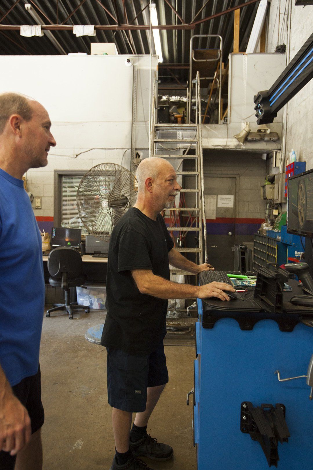 Two men examining machinery in a workshop, with a blue workbench in the foreground