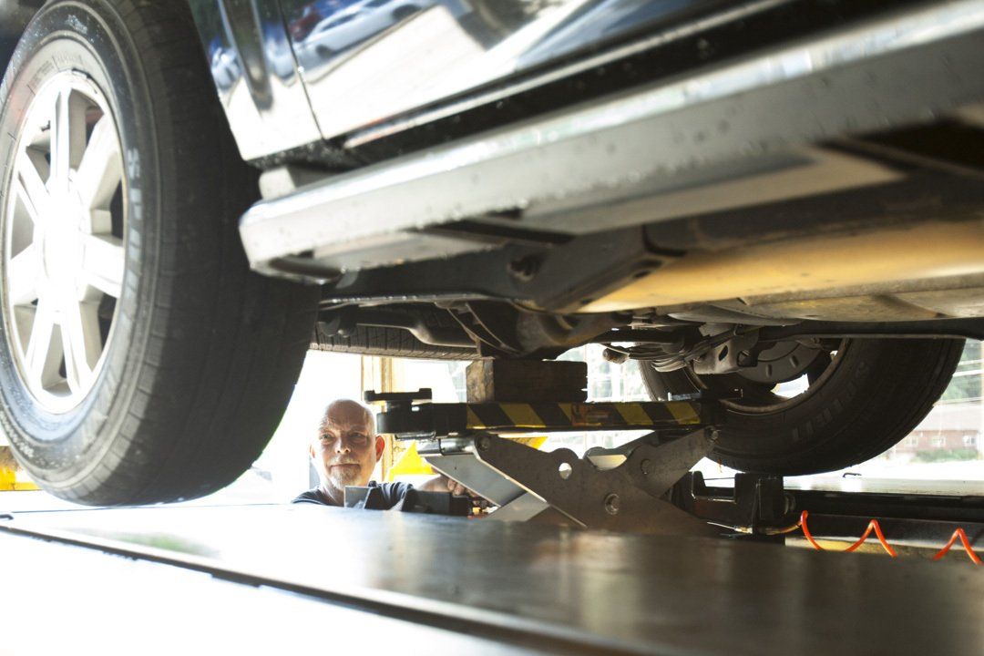 Car lifted on a service jack in a garage, with a mechanic visible underneath.