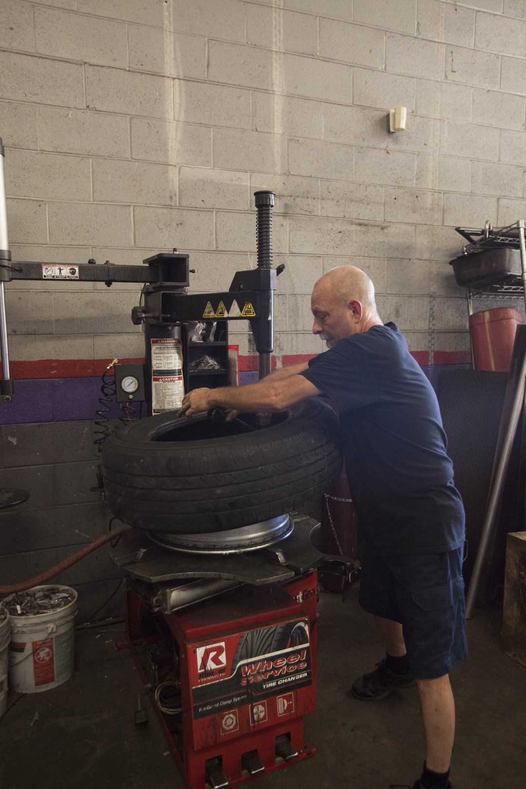 Mechanic leaning over a tire in an auto shop, beside a red tire-changing machine and oil cans