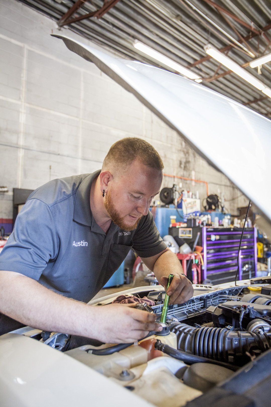 Mechanic working under a raised car in a garage, focused on engine repairs with tools nearby