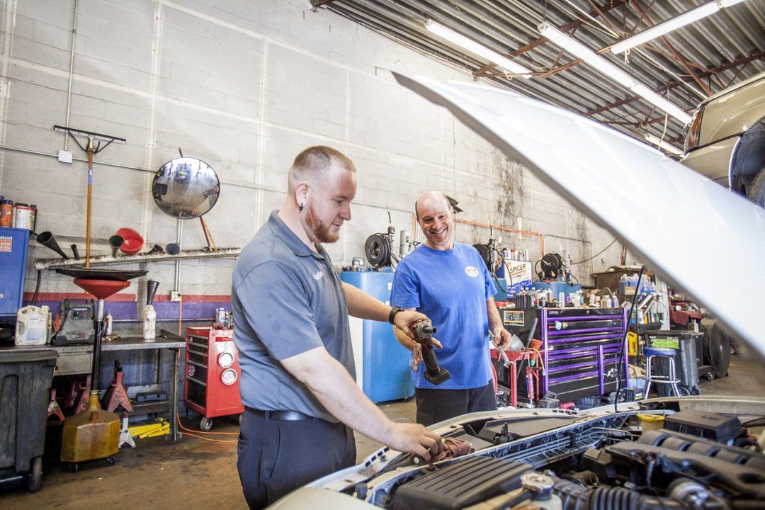Two people working on a car engine in a garage, with tools and equipment around them.
