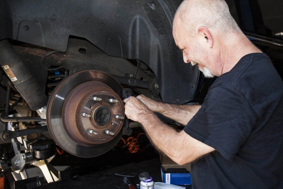 Mechanic working on a car’s exposed brake rotor in a garage