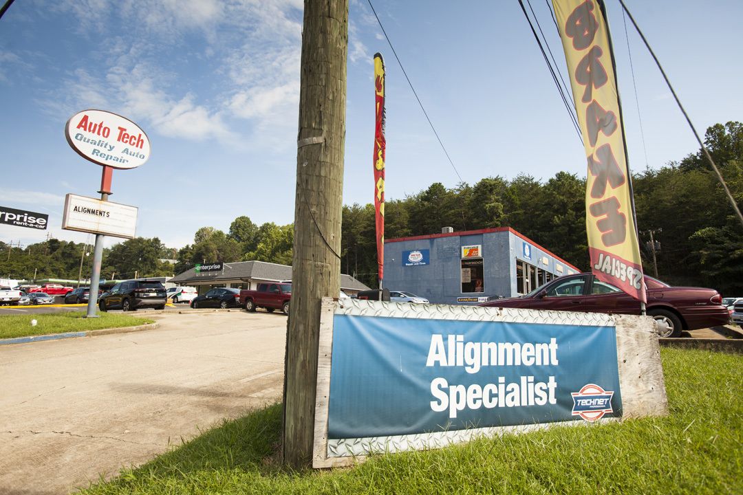 Auto alignment shop with blue sign, utility poles, parked cars, and a maroon vehicle by the road.
