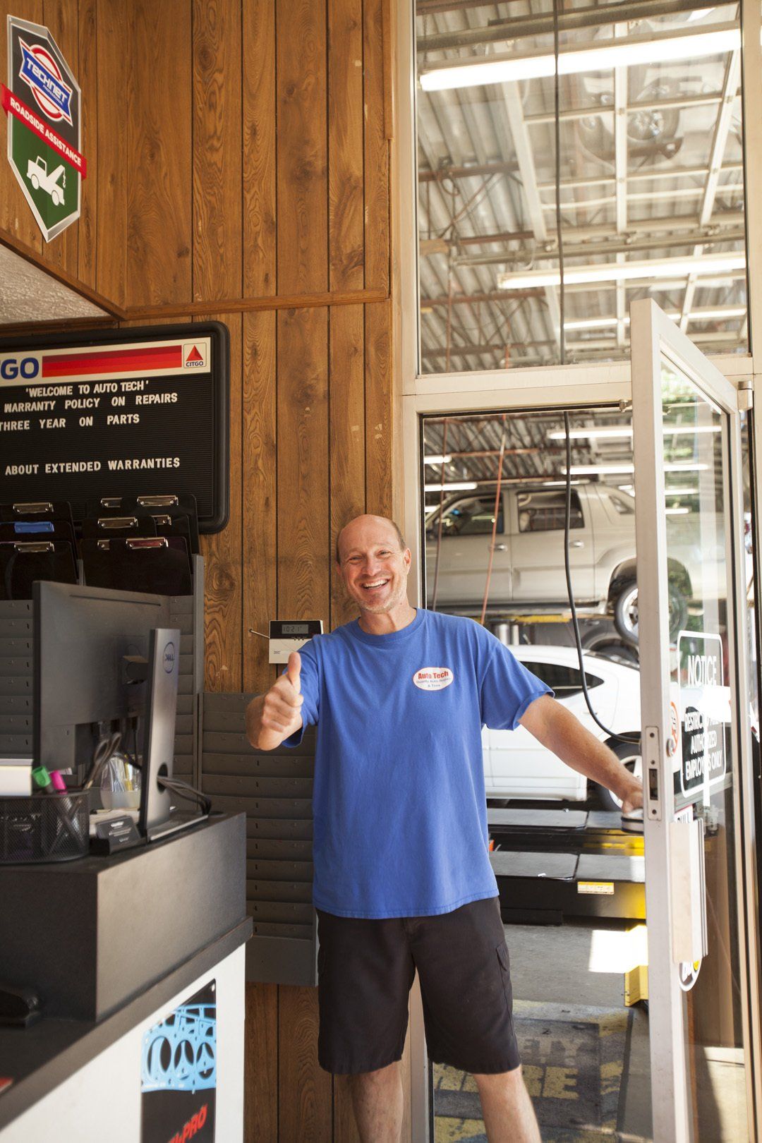 Man in blue shirt giving a thumbs-up at a doorway inside a garage or shop