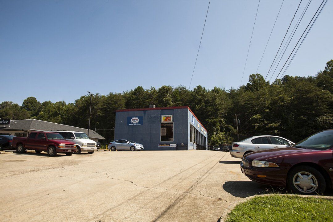 Small blue building with parked cars beside a dirt lot and trees under power lines