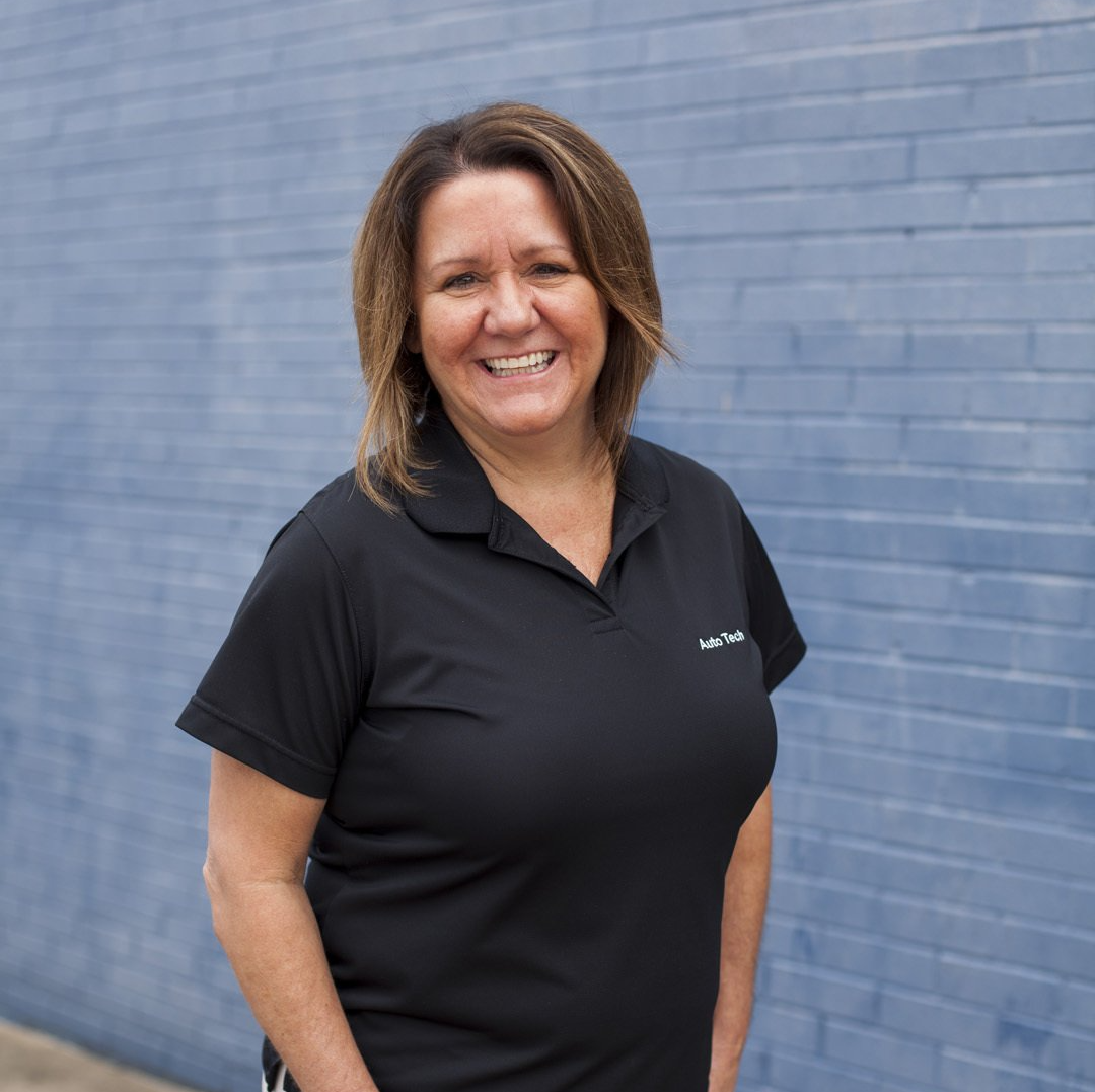 Smiling woman in a black polo standing against a blue brick wall