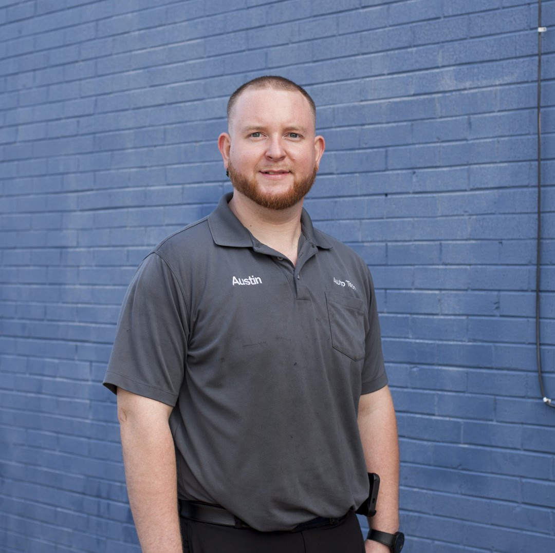 Man standing in a gray polo against a blue brick wall, facing the camera and smiling.