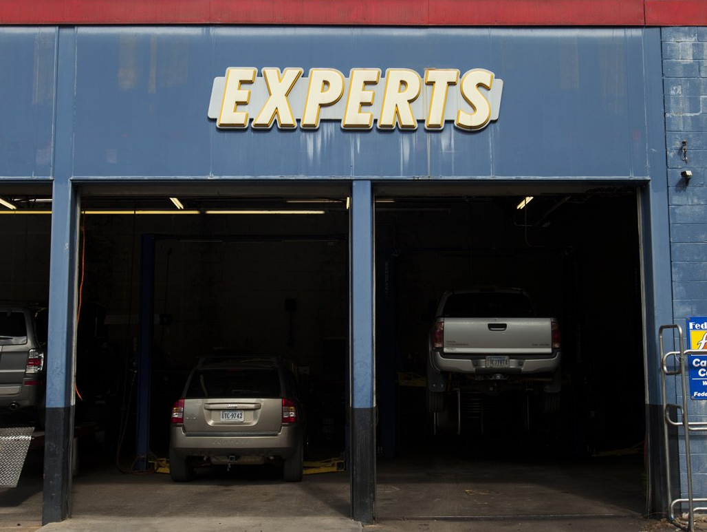 Auto repair garage with blue facade and three open bays, two cars parked inside under an “EXPERTS” sign