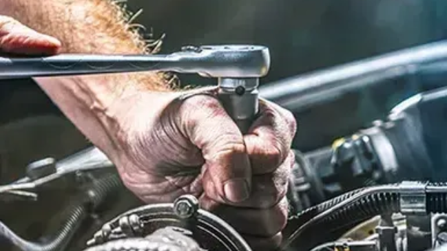 Hand tightening a bolt on a car engine with a socket wrench, close-up.