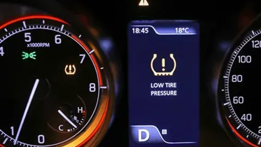 Car dashboard shows low tire pressure warning on center display, with speedometer gauges lit in red.