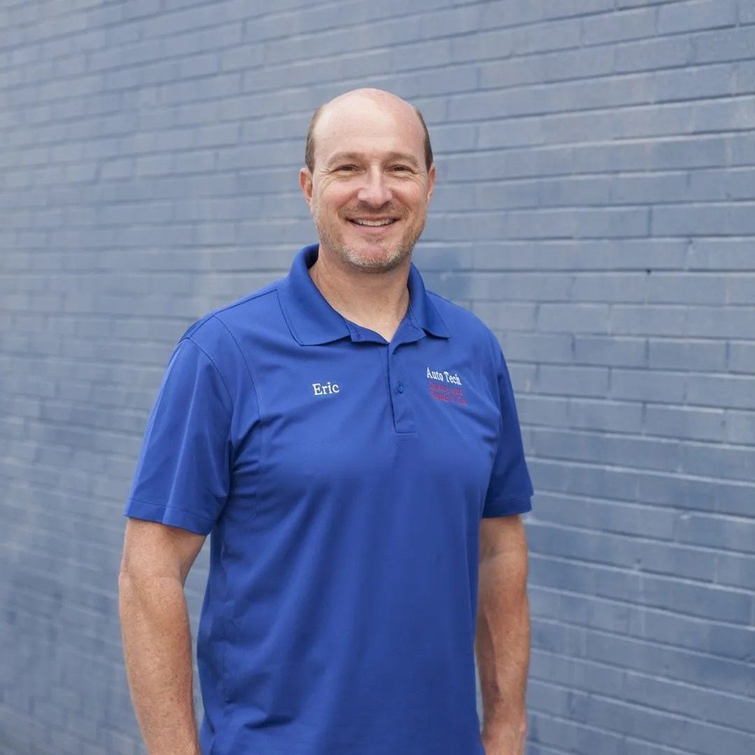 Smiling man in a blue polo standing against a gray brick wall