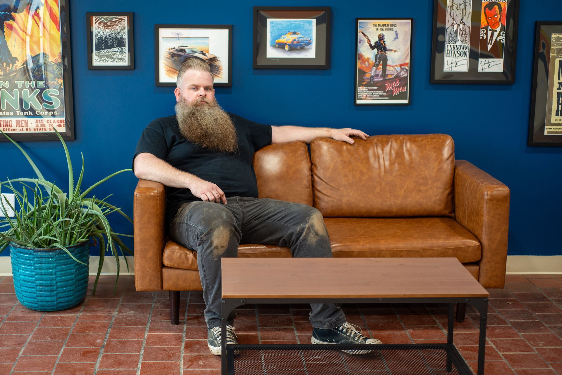 A man with a beard is sitting on a brown leather couch.