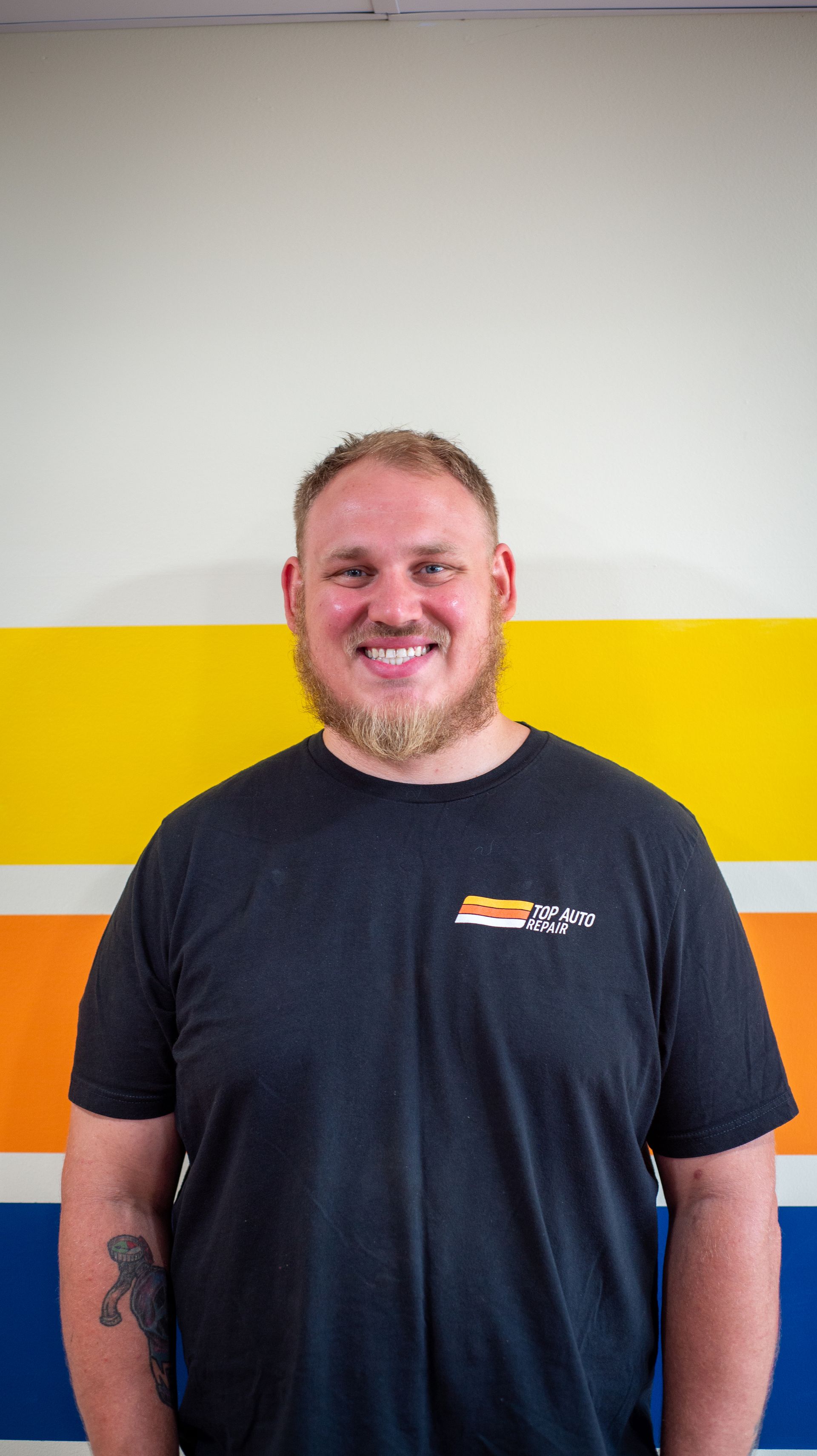 A man with a beard is wearing a black t-shirt and smiling. | Top Auto Repair