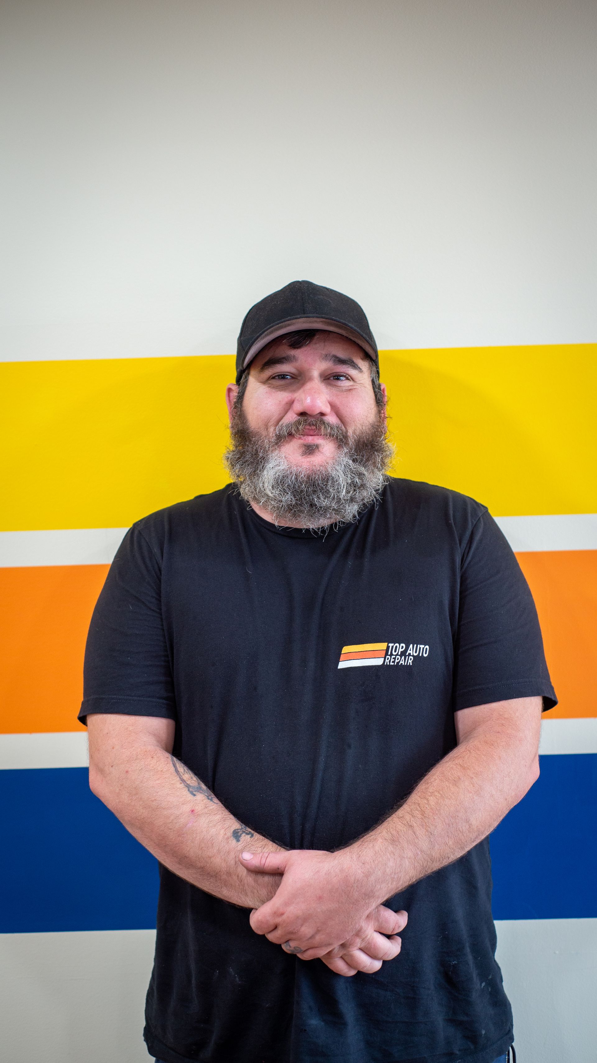 A man with a beard is standing in front of a colorful wall. | Top Auto Repair