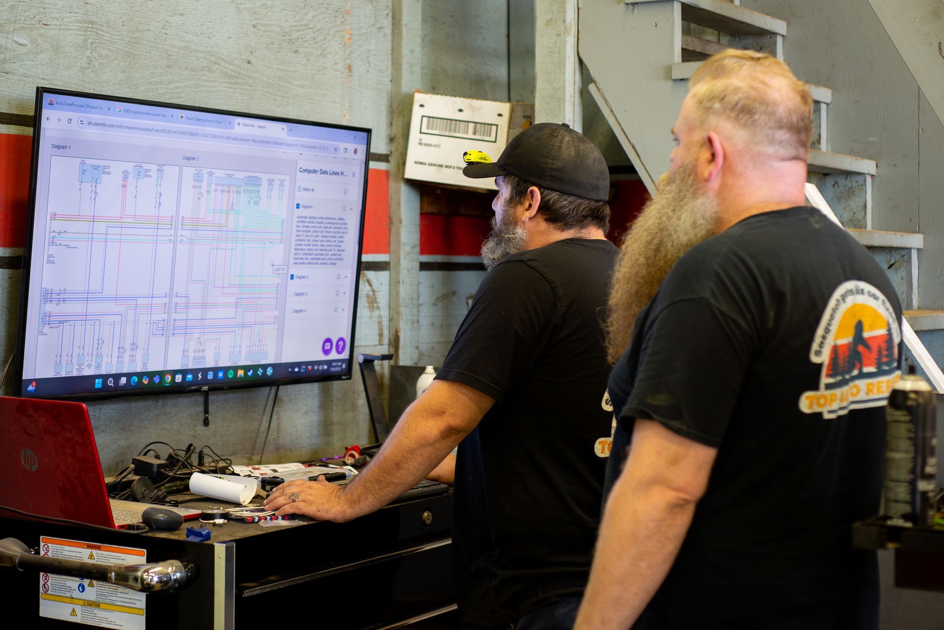 Two men are looking at a computer screen in a garage. | Top Auto Repair