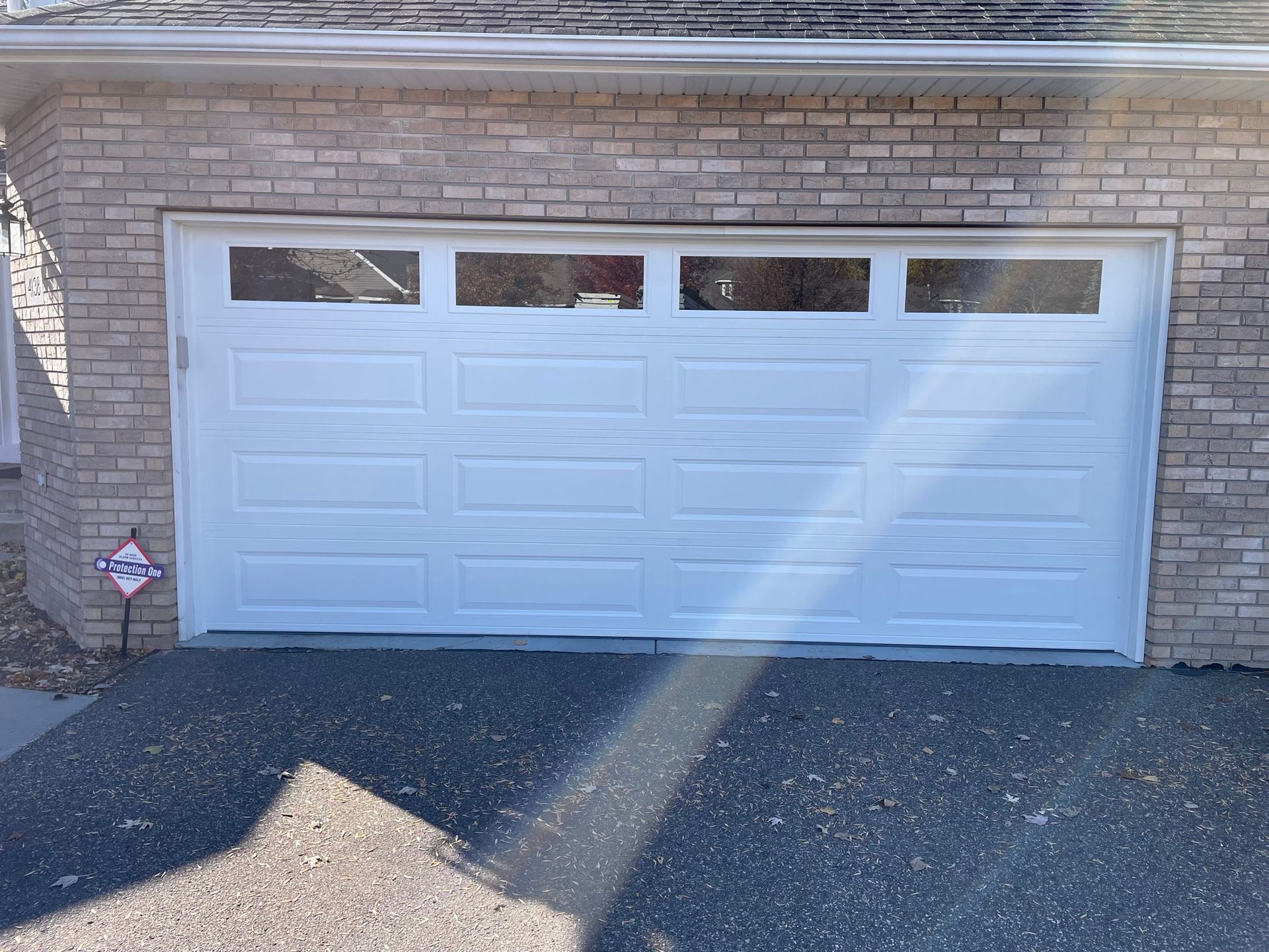 White garage door with glass panels, set in a brick wall, driveway in front.