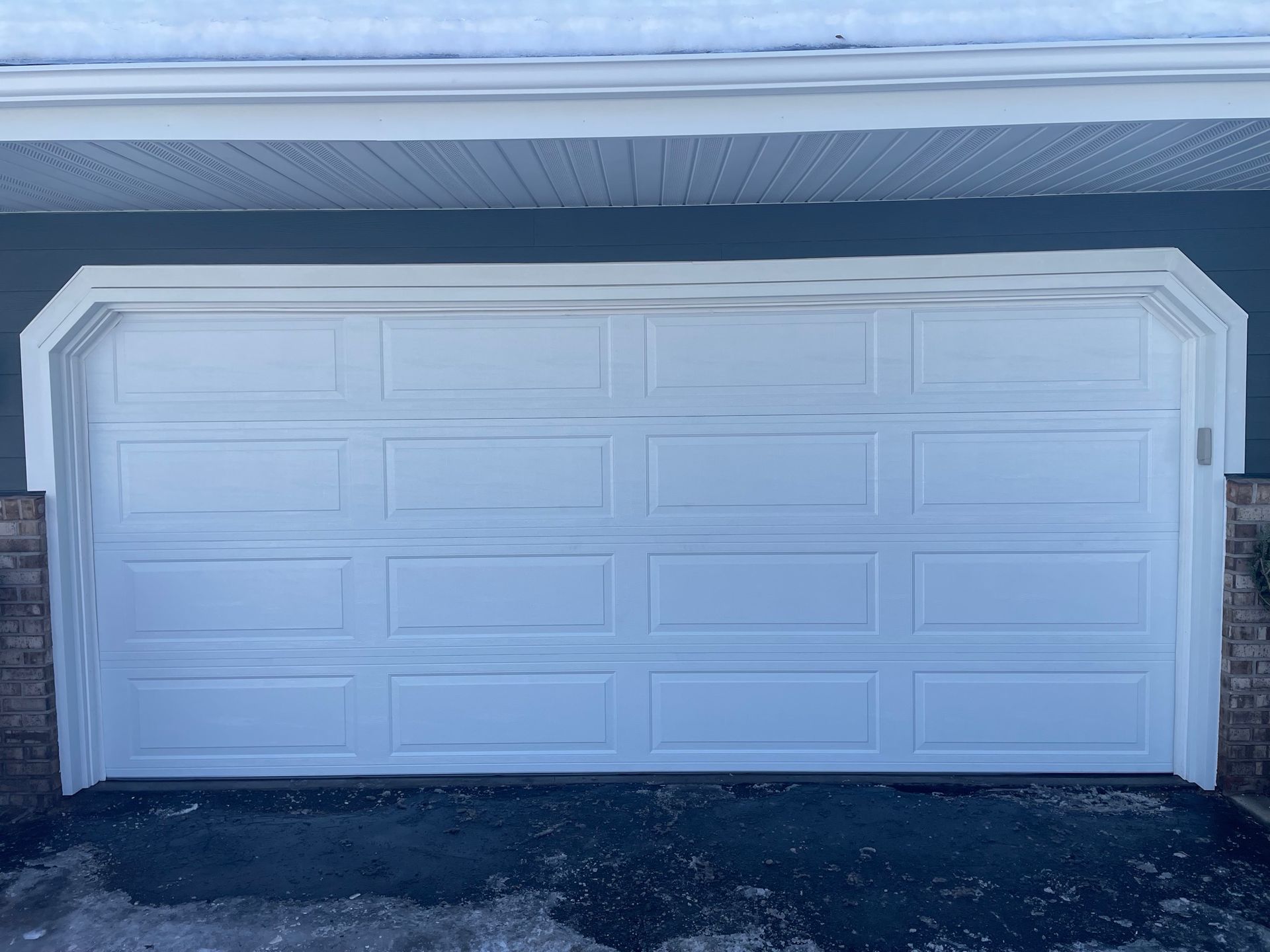 White garage door with rectangular panels, set in a light blue house with white trim.