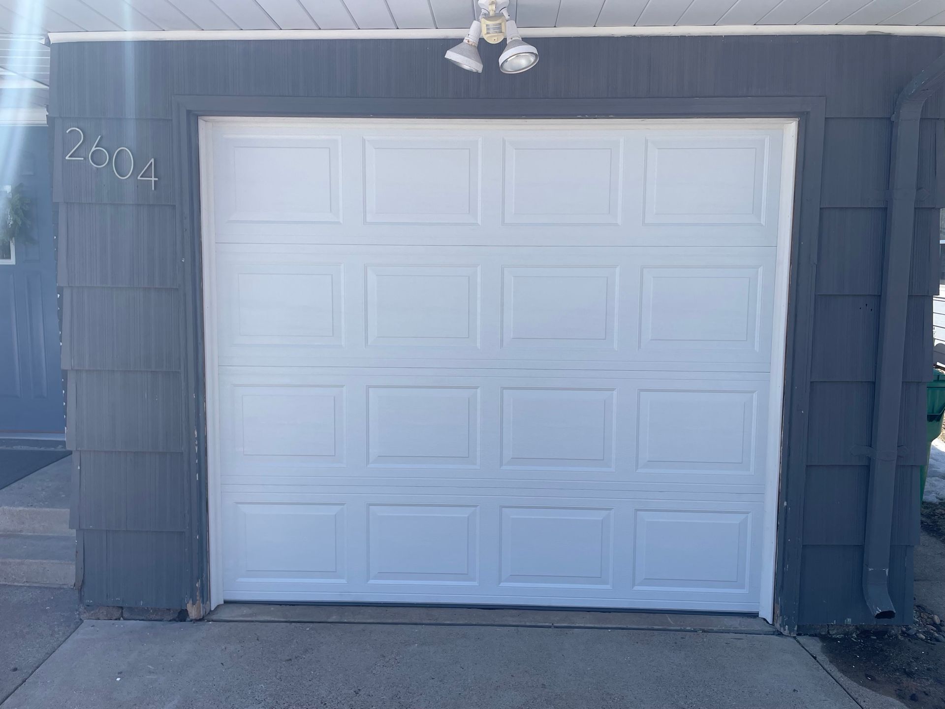 White garage door on a gray house, with address numbers visible.