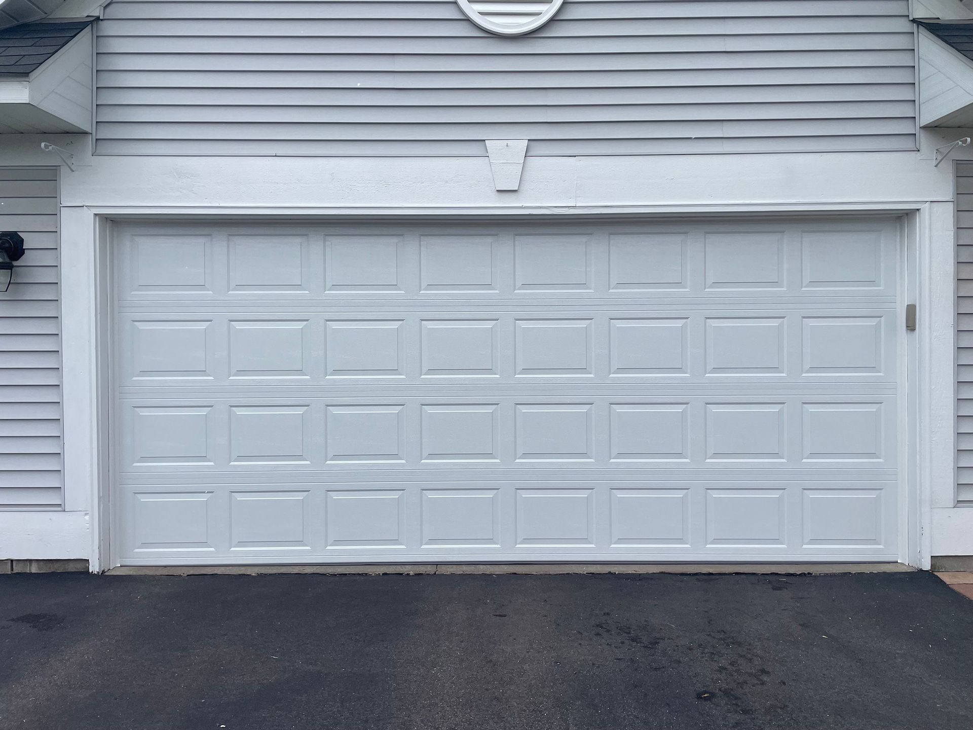 White garage door, closed, with asphalt driveway. Gray siding above.