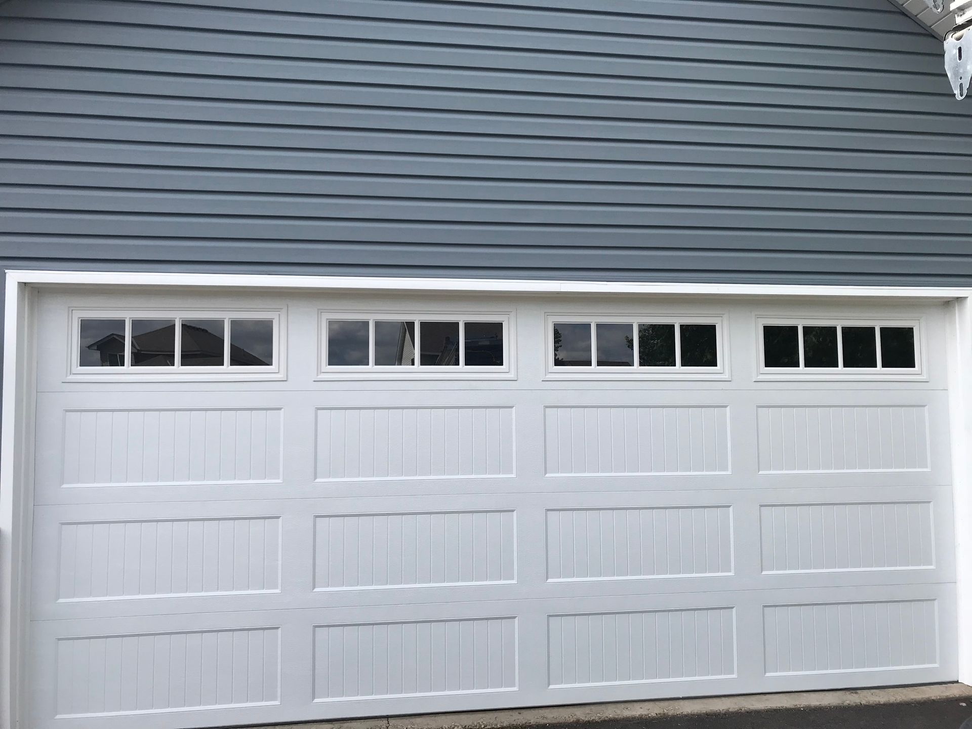 White garage door with four window panels above, set against blue siding.