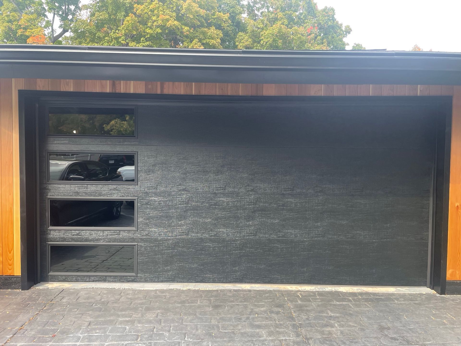 Black garage door with rectangular windows, flanked by wood siding.