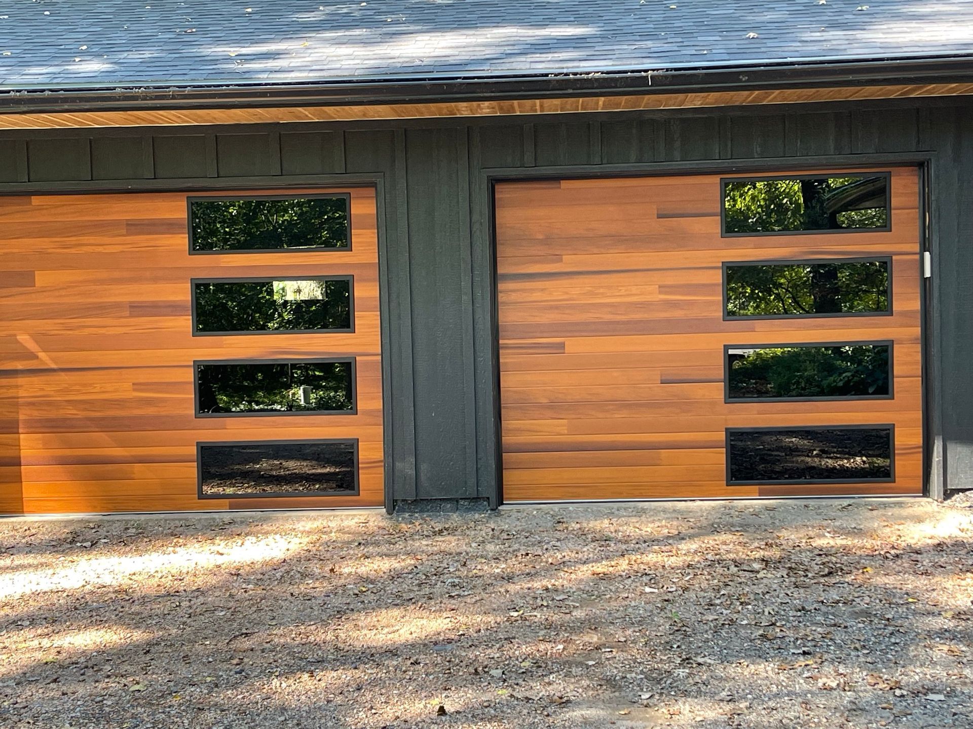 Two brown wooden garage doors with four rectangular windows each, set in a dark gray building.