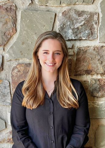Smiling woman in a bright green dress standing before a stone wall.
