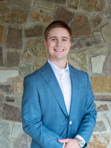 Man in a blue blazer smiling in front of a stone wall