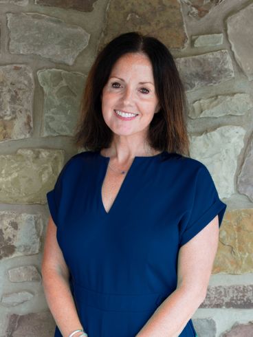 Smiling woman in a navy jumpsuit standing before a stone wall.