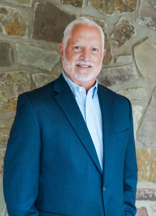 Smiling man in a blue blazer standing in front of a stone wall