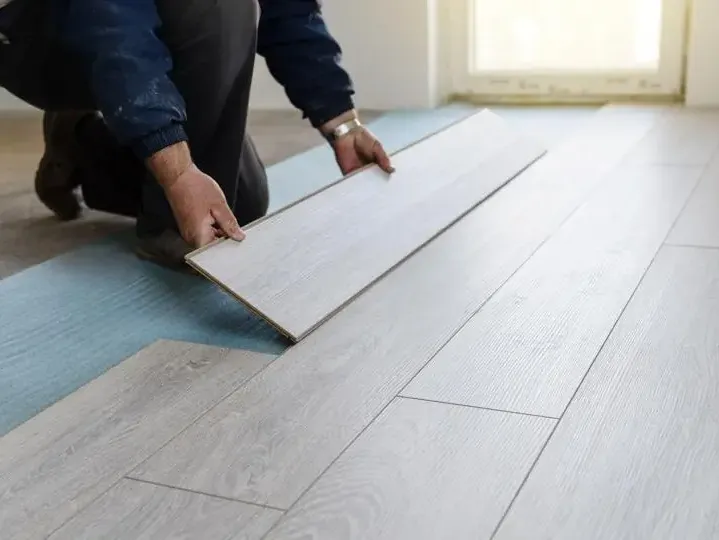 A man is installing a wooden floor in a room.