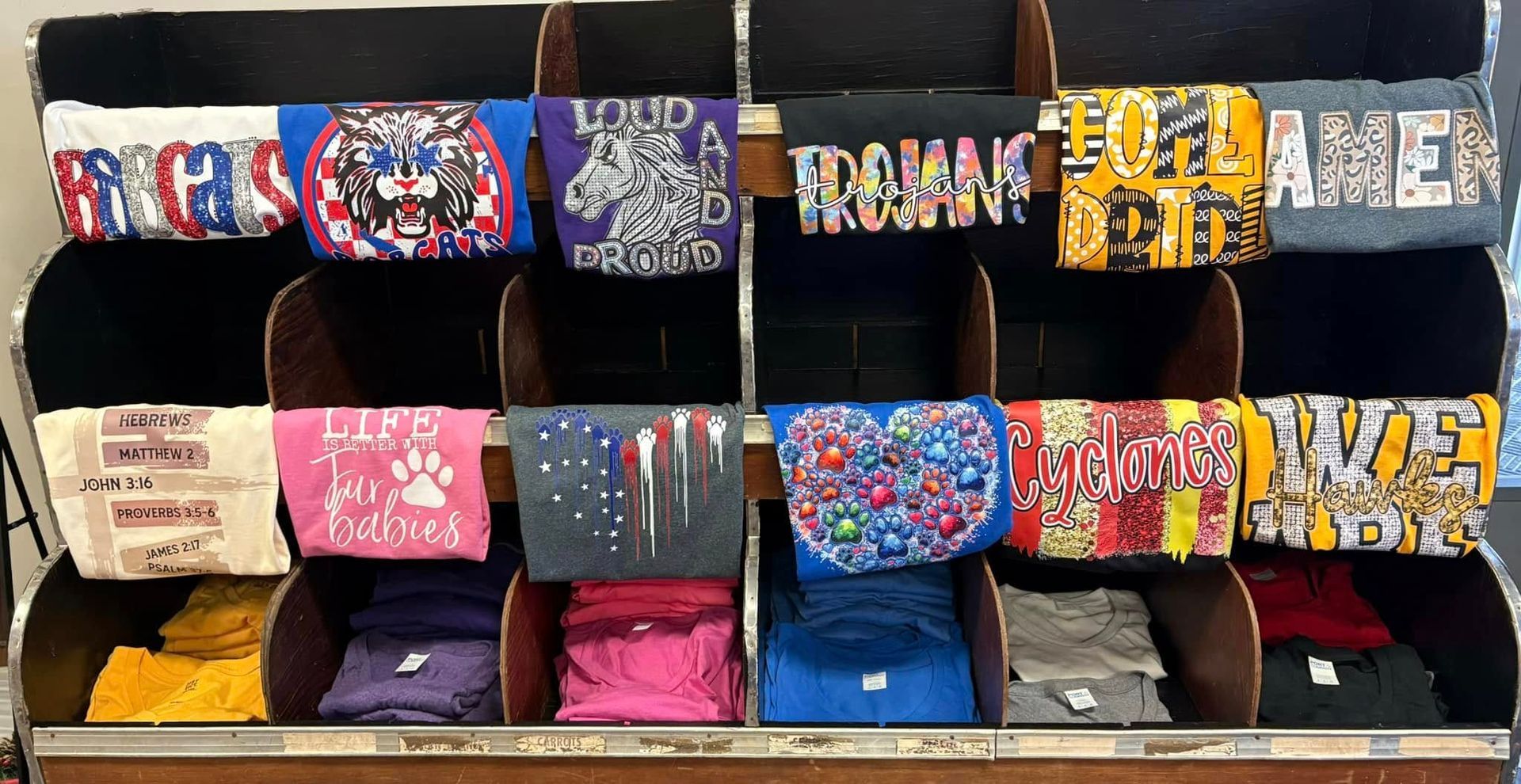 A retail display rack featuring folded graphic t-shirts organized on three shelves in rows.