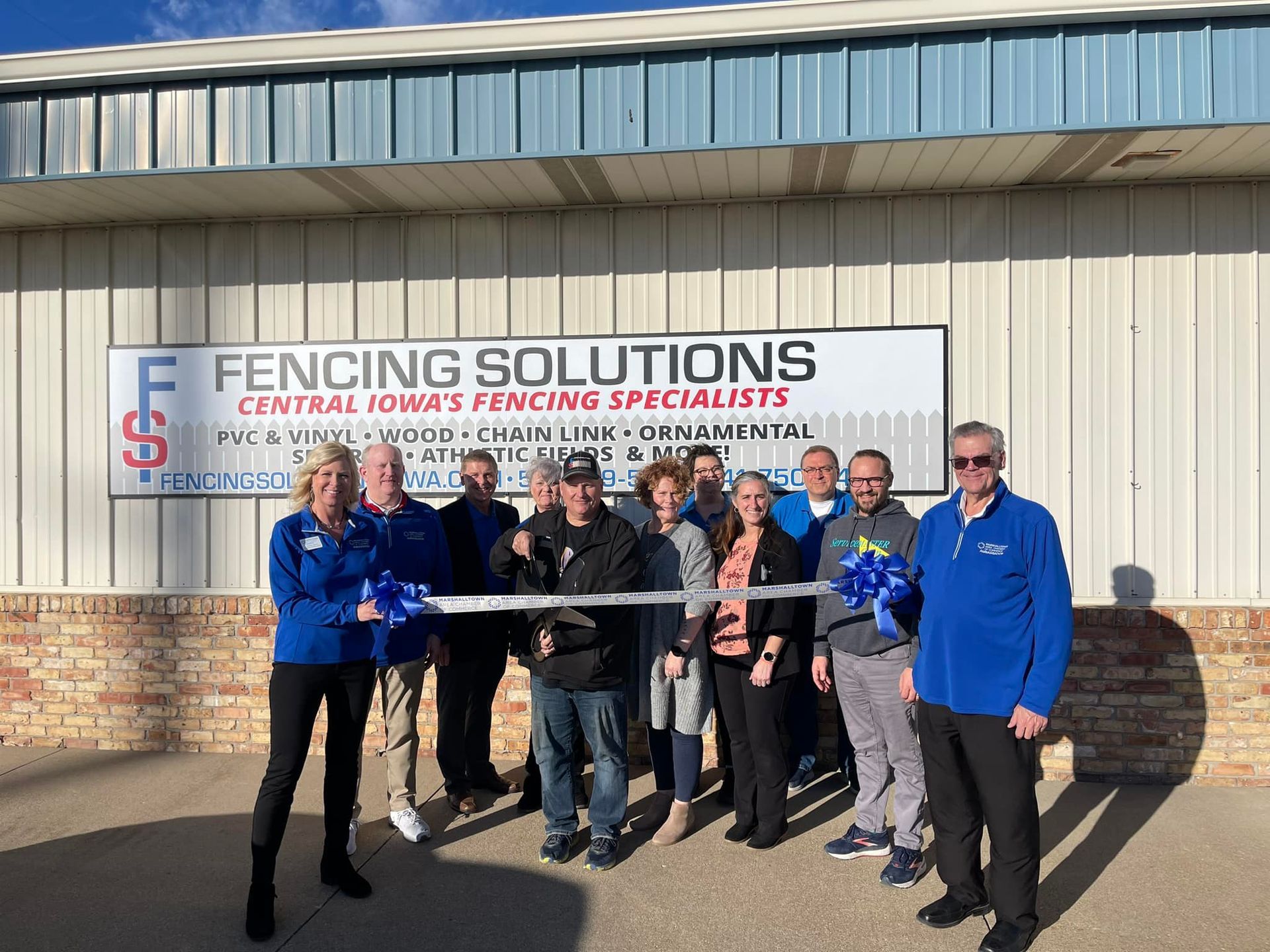 A group of people standing outside Fencing Solutions for a ribbon-cutting ceremony in front of their company sign.