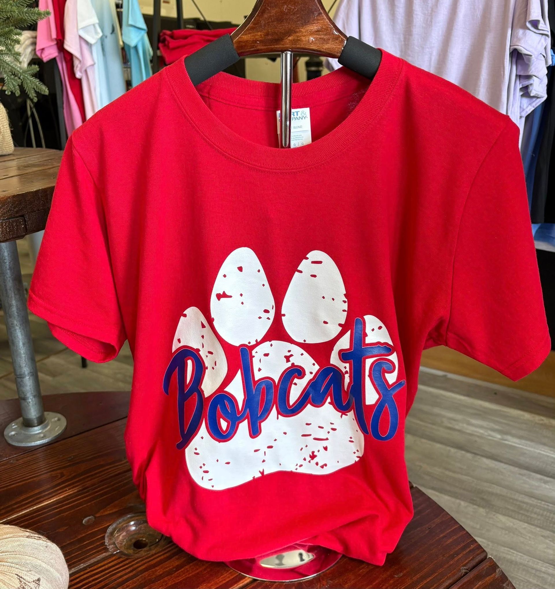 Red t-shirt hanging on a display, featuring a distressed white paw print graphic with 