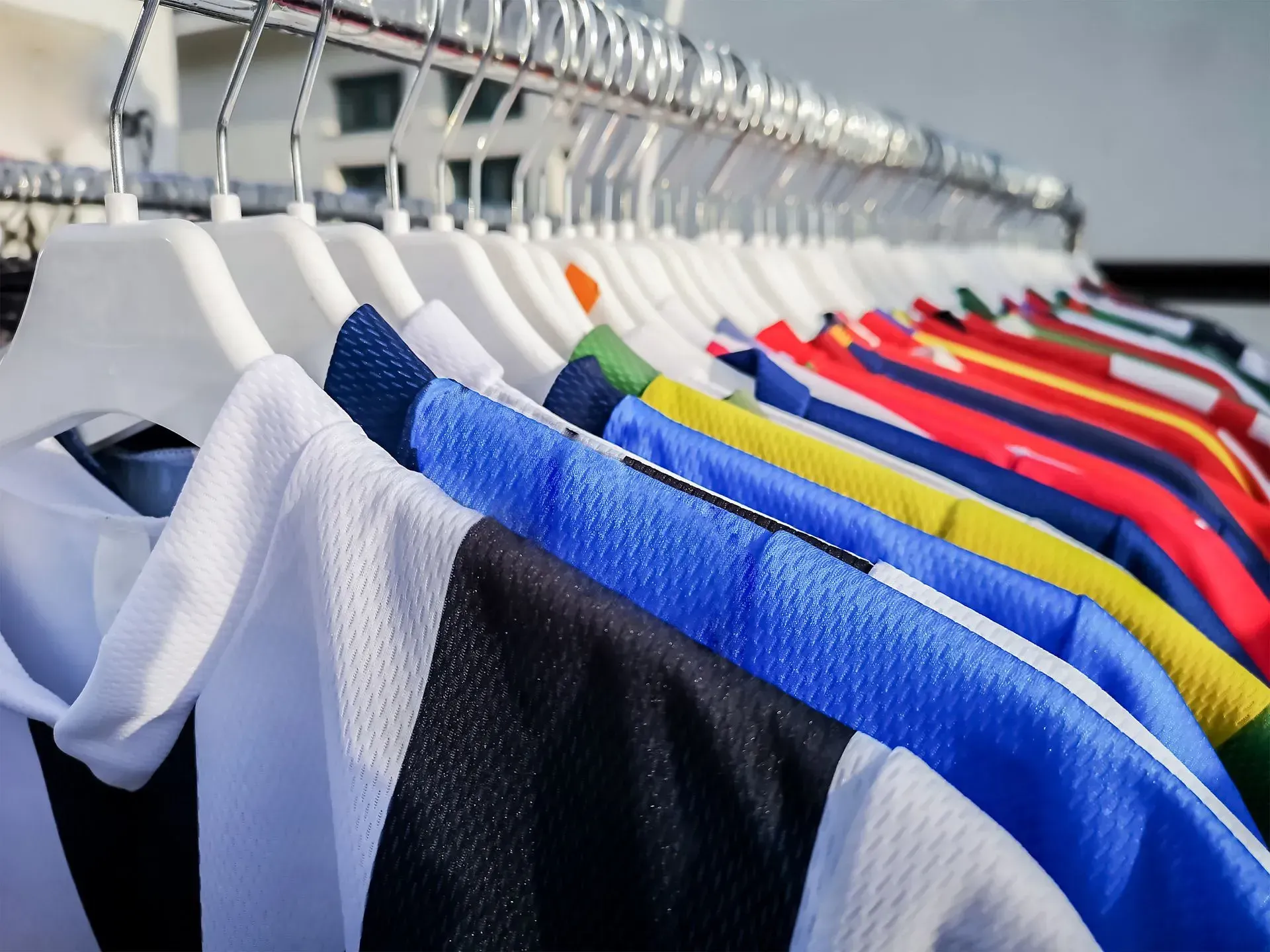 A row of various colorful sports jerseys hanging on white hangers on a clothing rack.