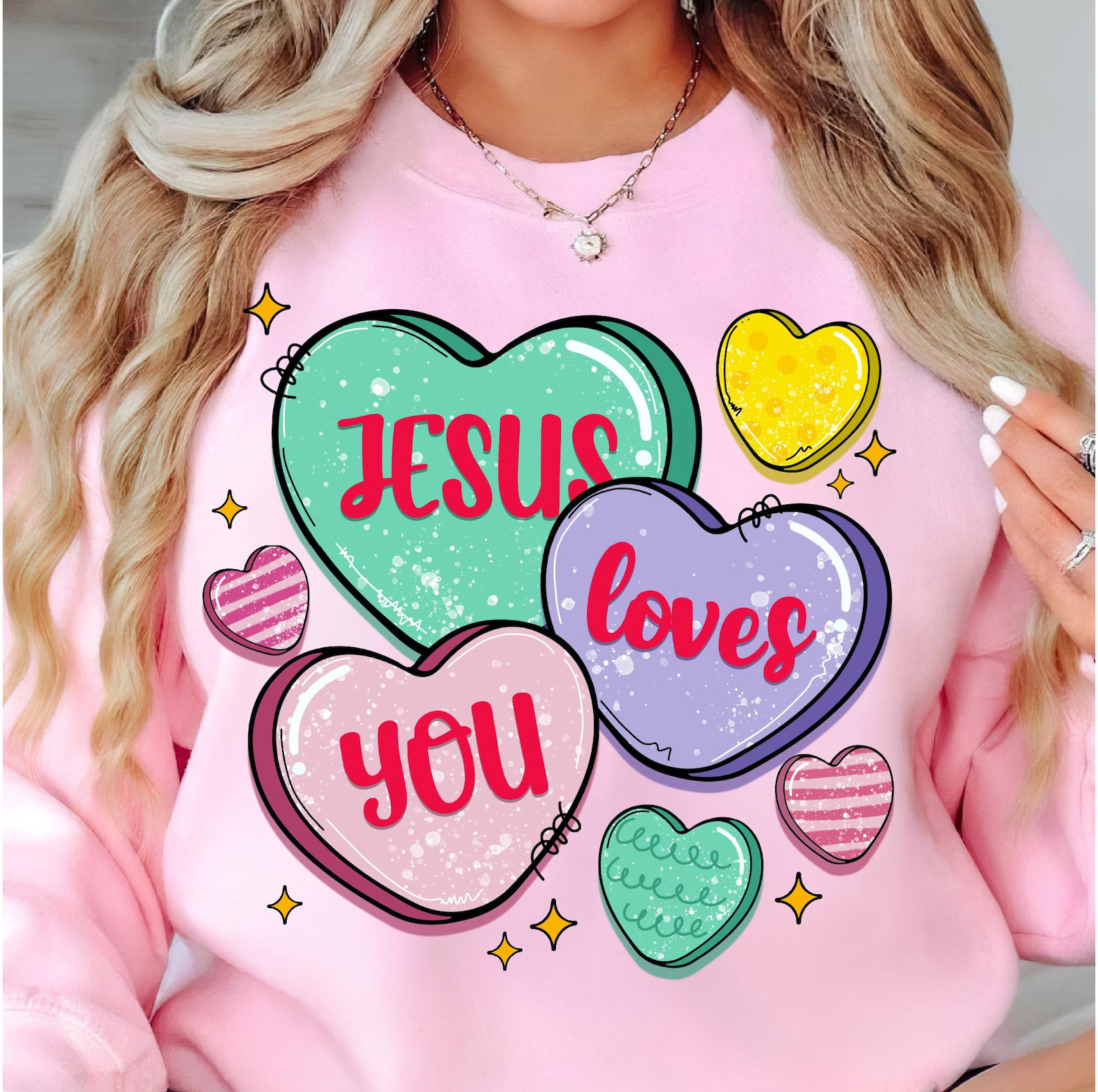 A person wears a light pink sweatshirt featuring three large heart-shaped candies with the text 