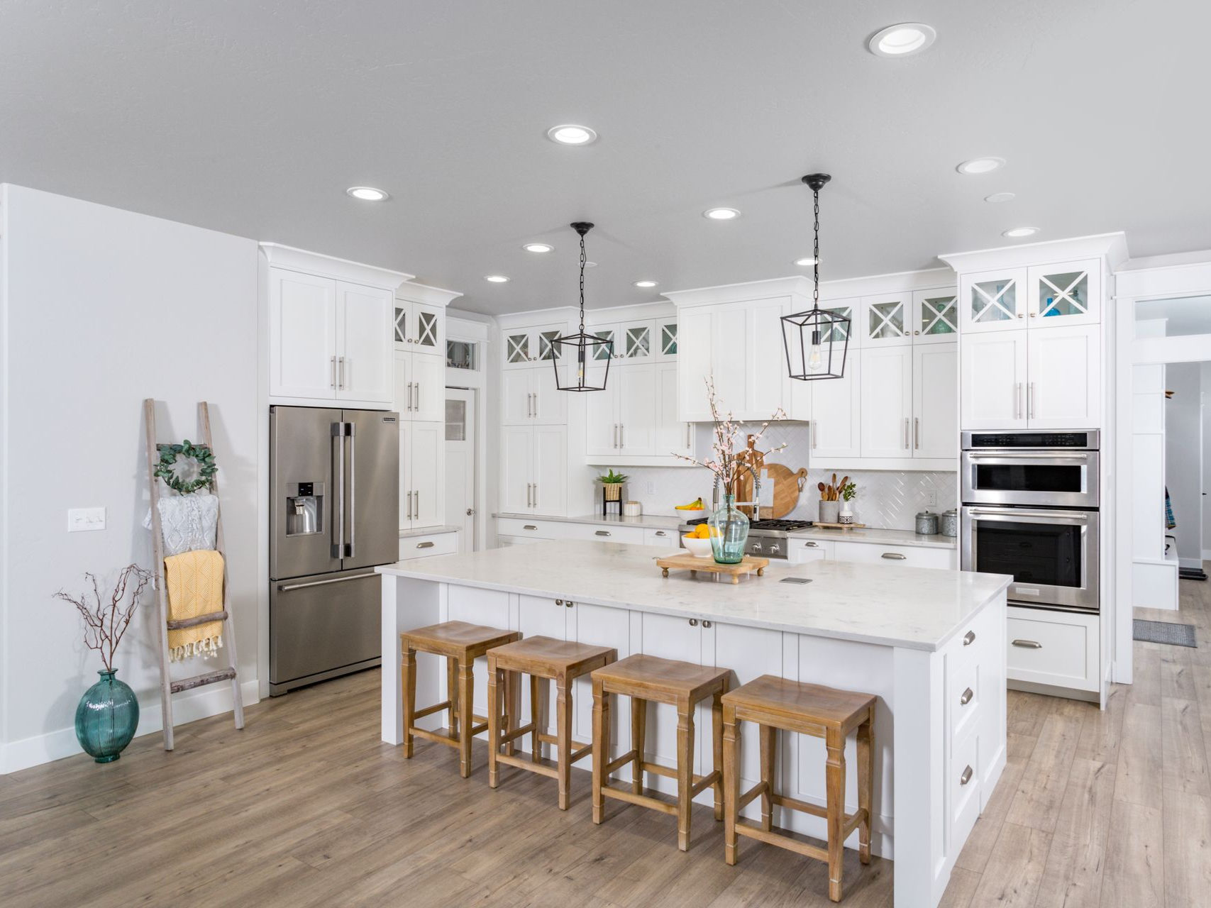 A modern kitchen features white cabinetry, a marble-topped island with four wooden stools, and stainless steel appliances.