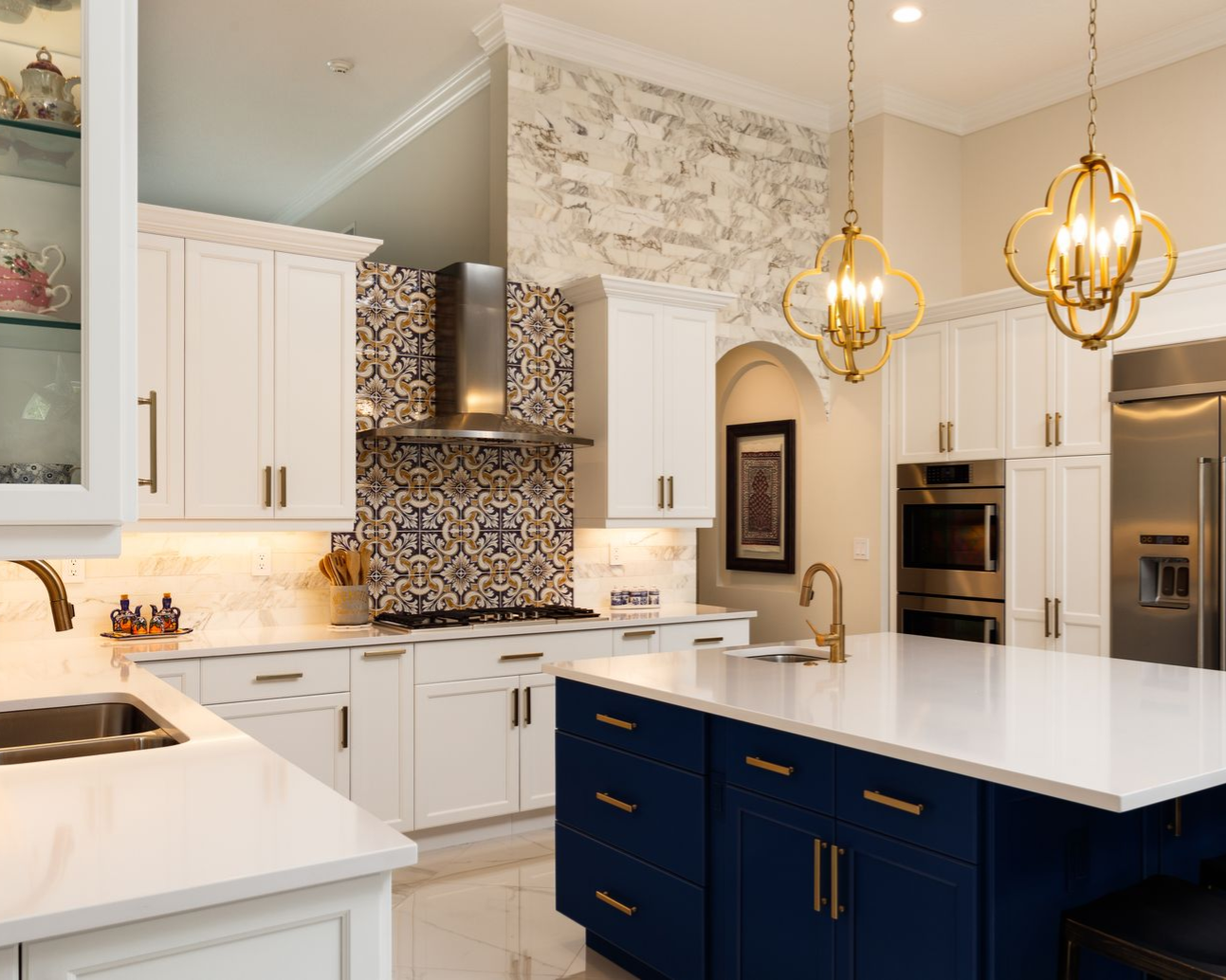 A luxury kitchen with a white marble island, blue cabinets, white cabinetry, decorative tile backsplash, and two pendants.