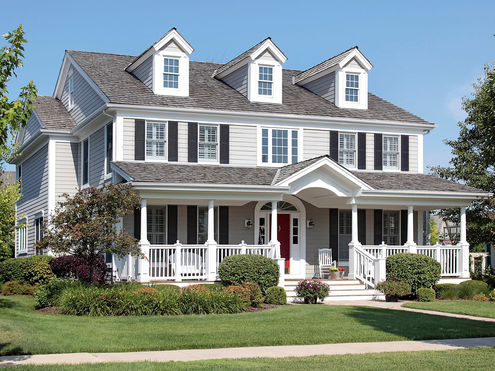 A two-story gray house with a wide front porch, dark shutters, three gabled dormers, and a prominent red front door.check mark icon