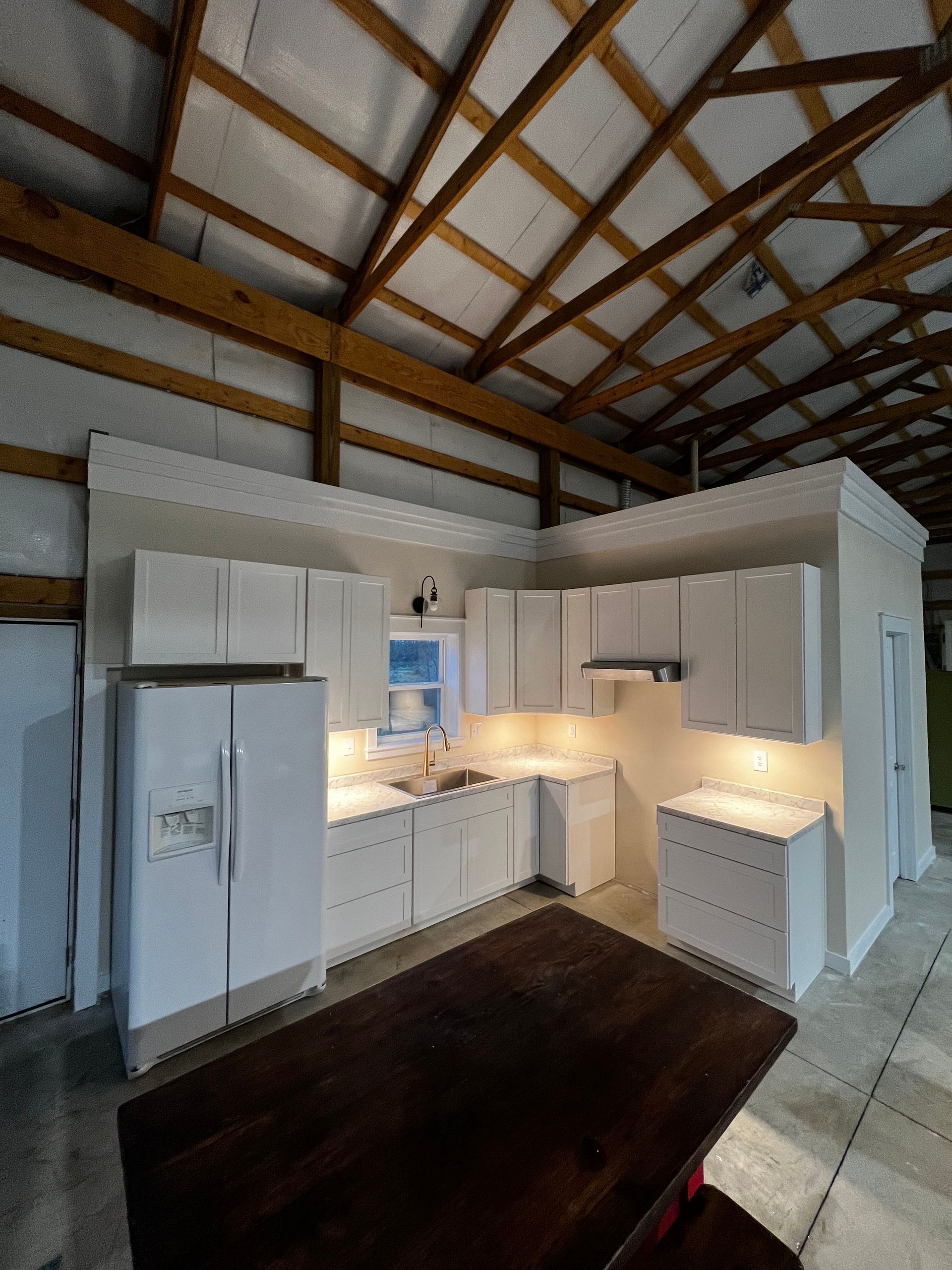 White kitchen with vaulted wood-beam ceiling, stainless fridge, and dark wood island in a bright cabin interior