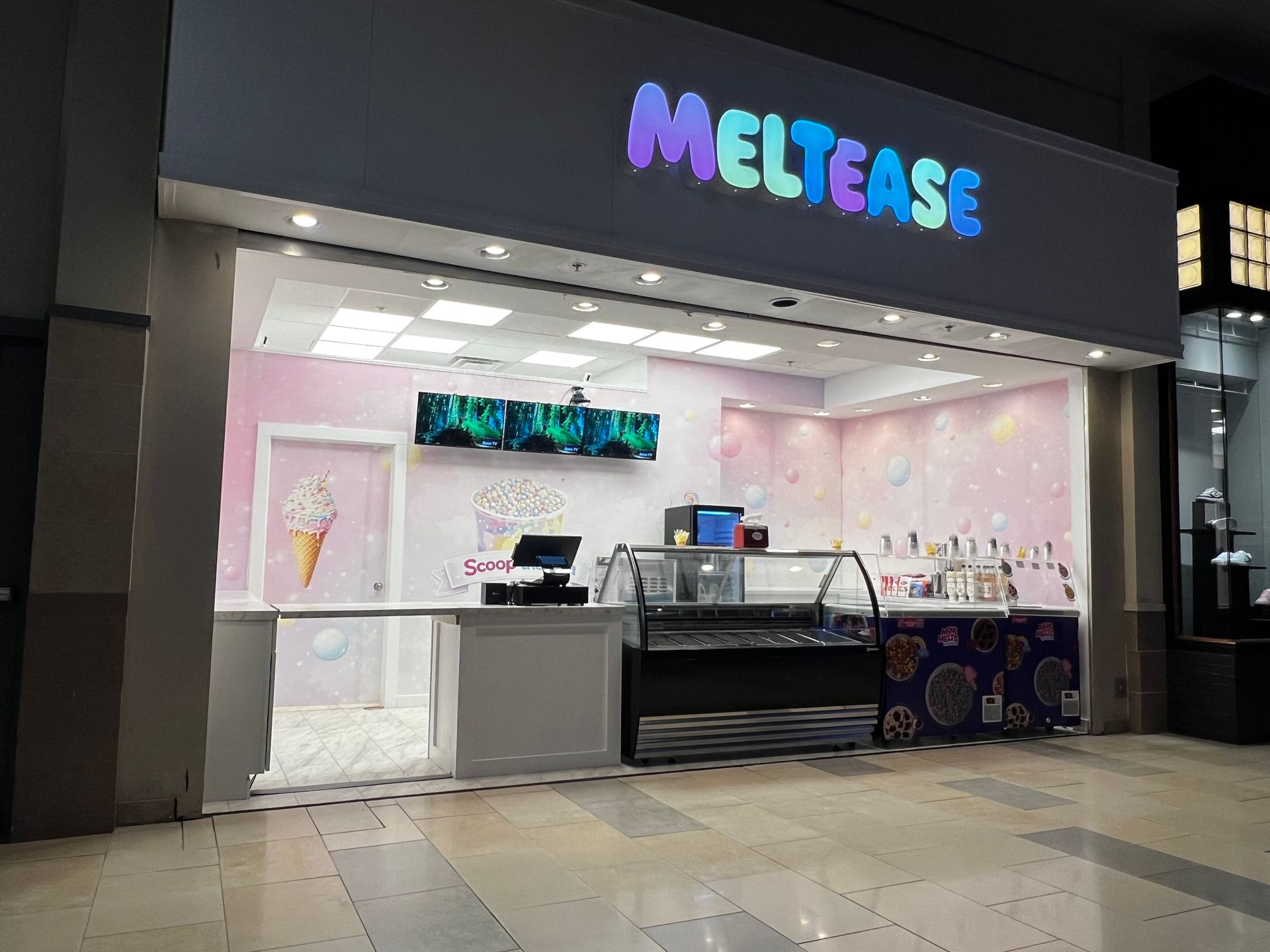 Storefront of a MELTEASE bubble tea shop with a black sign and pink-lit interior in a mall.