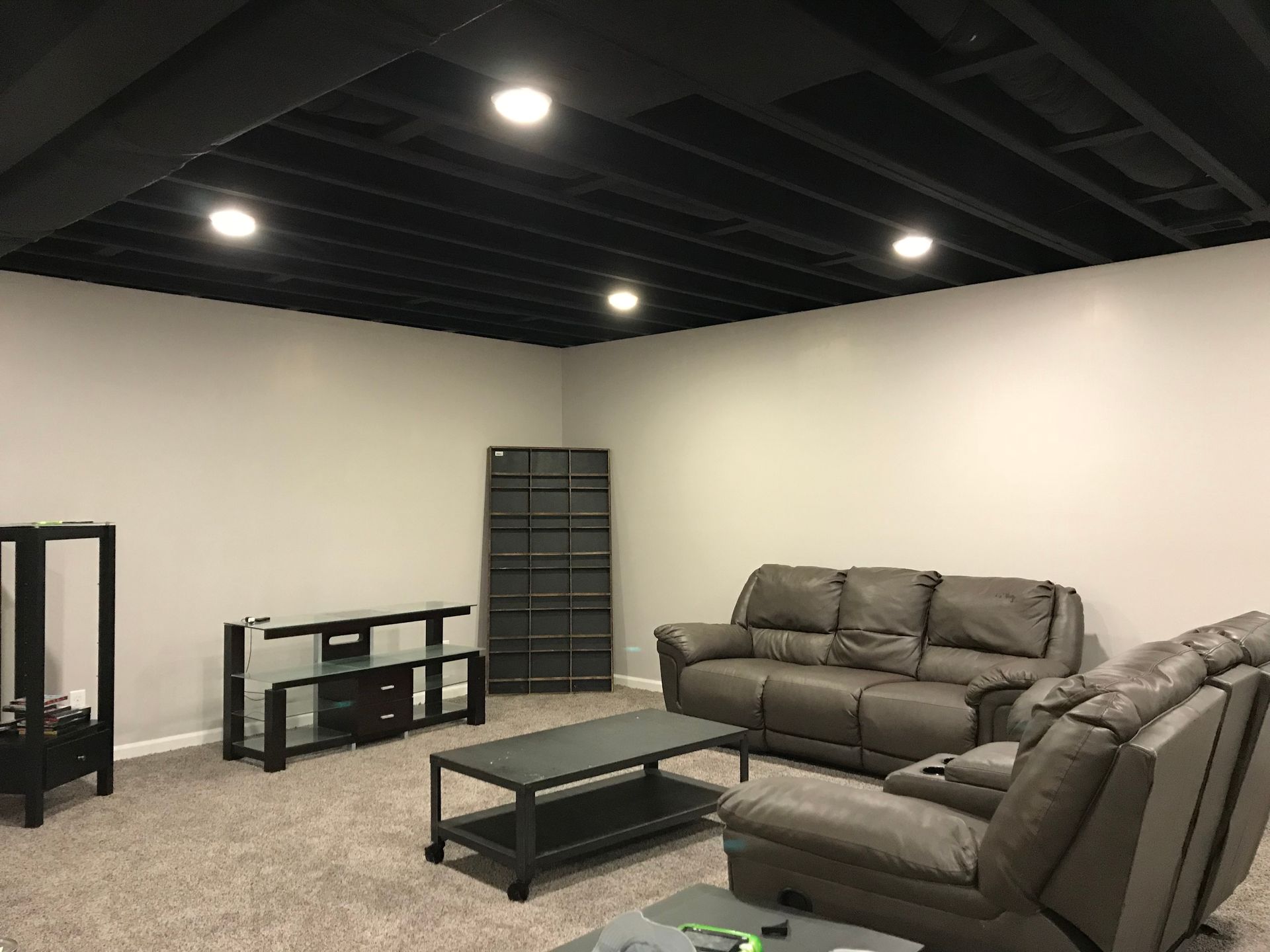 Basement living room with gray sofa, coffee table, desk, shelf, and recessed ceiling lights