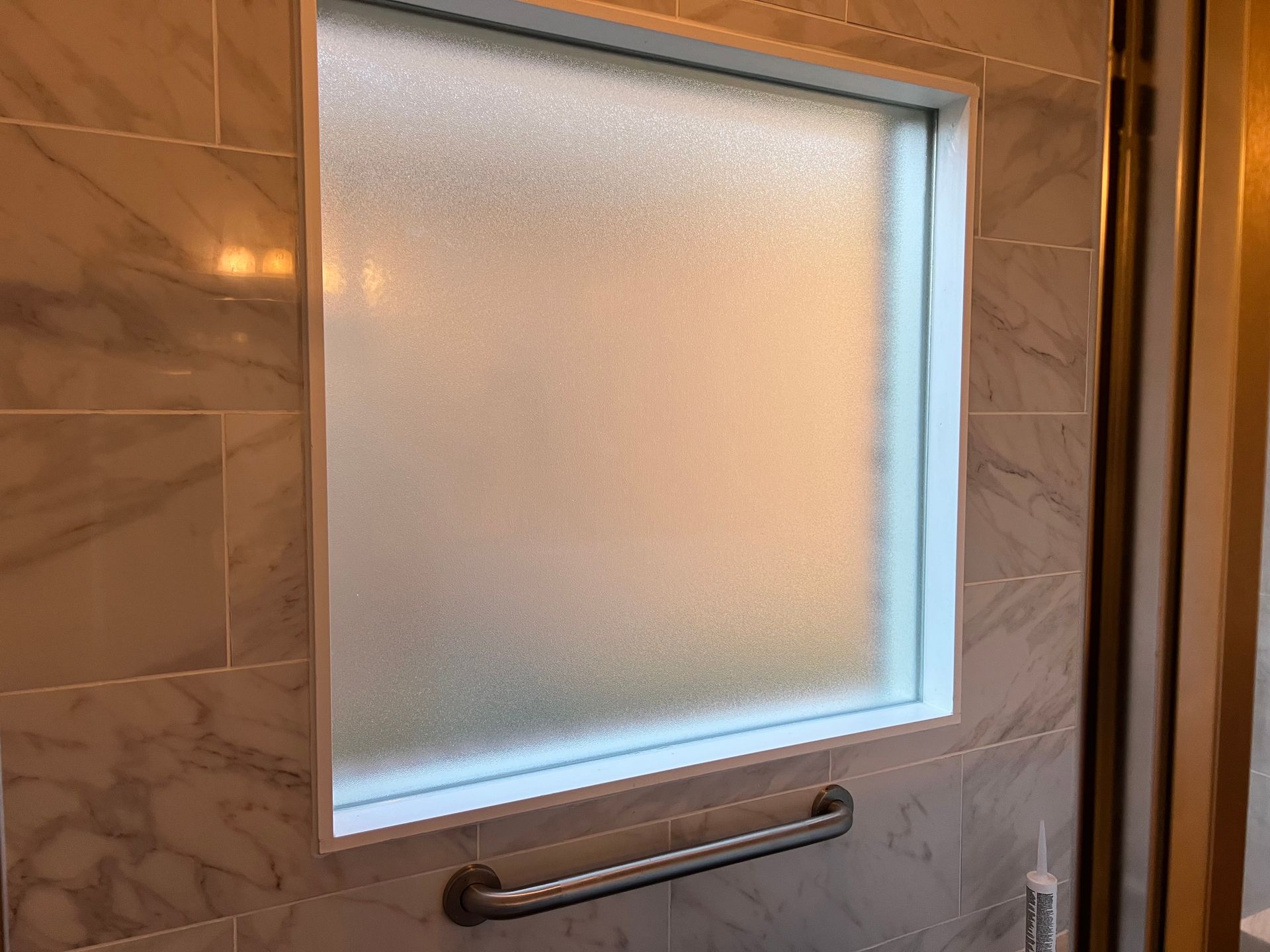 Frosted glass shower window with a metal grab bar in a tiled bathroom