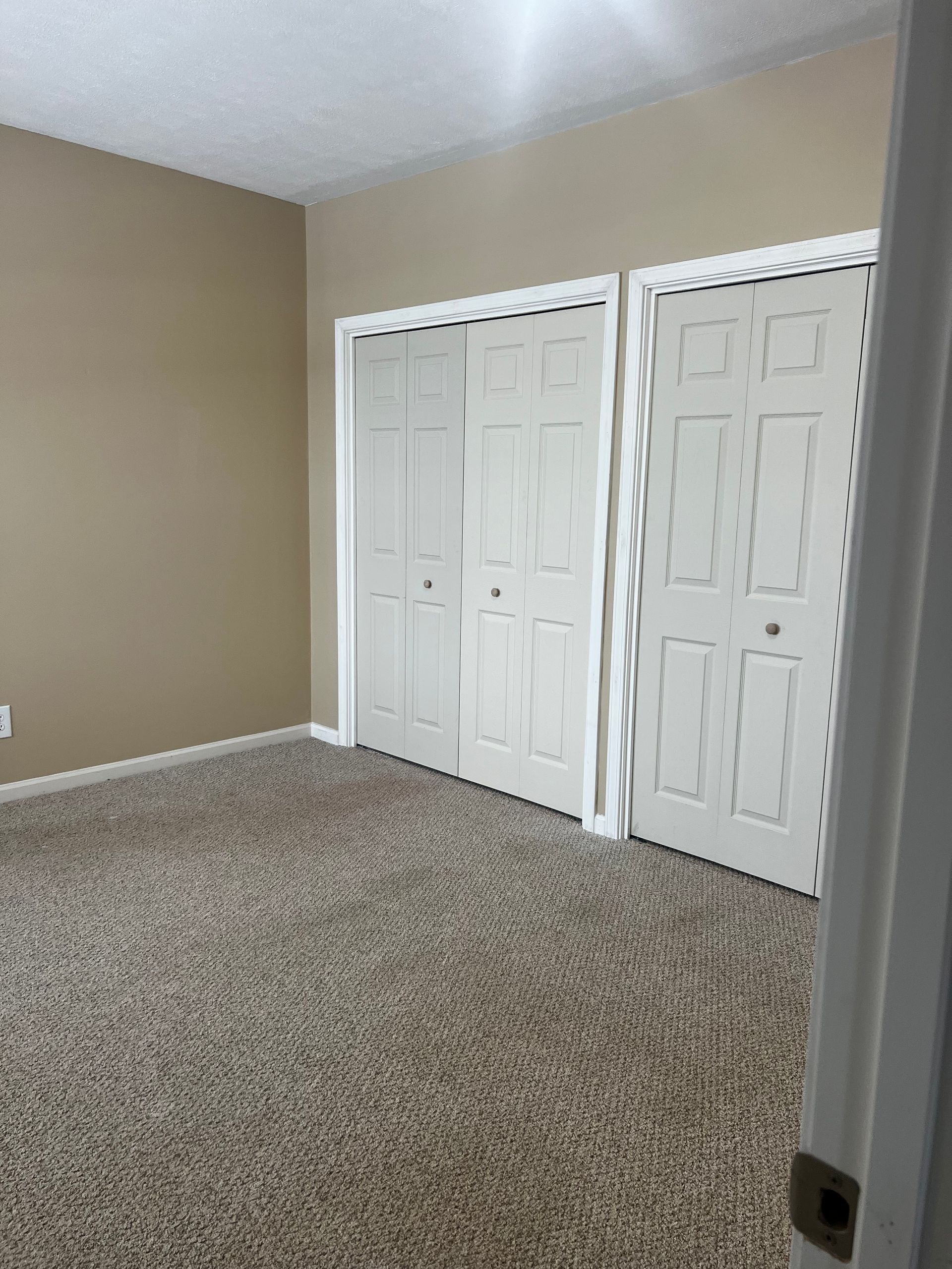 Empty beige bedroom with carpet and two white closet doors