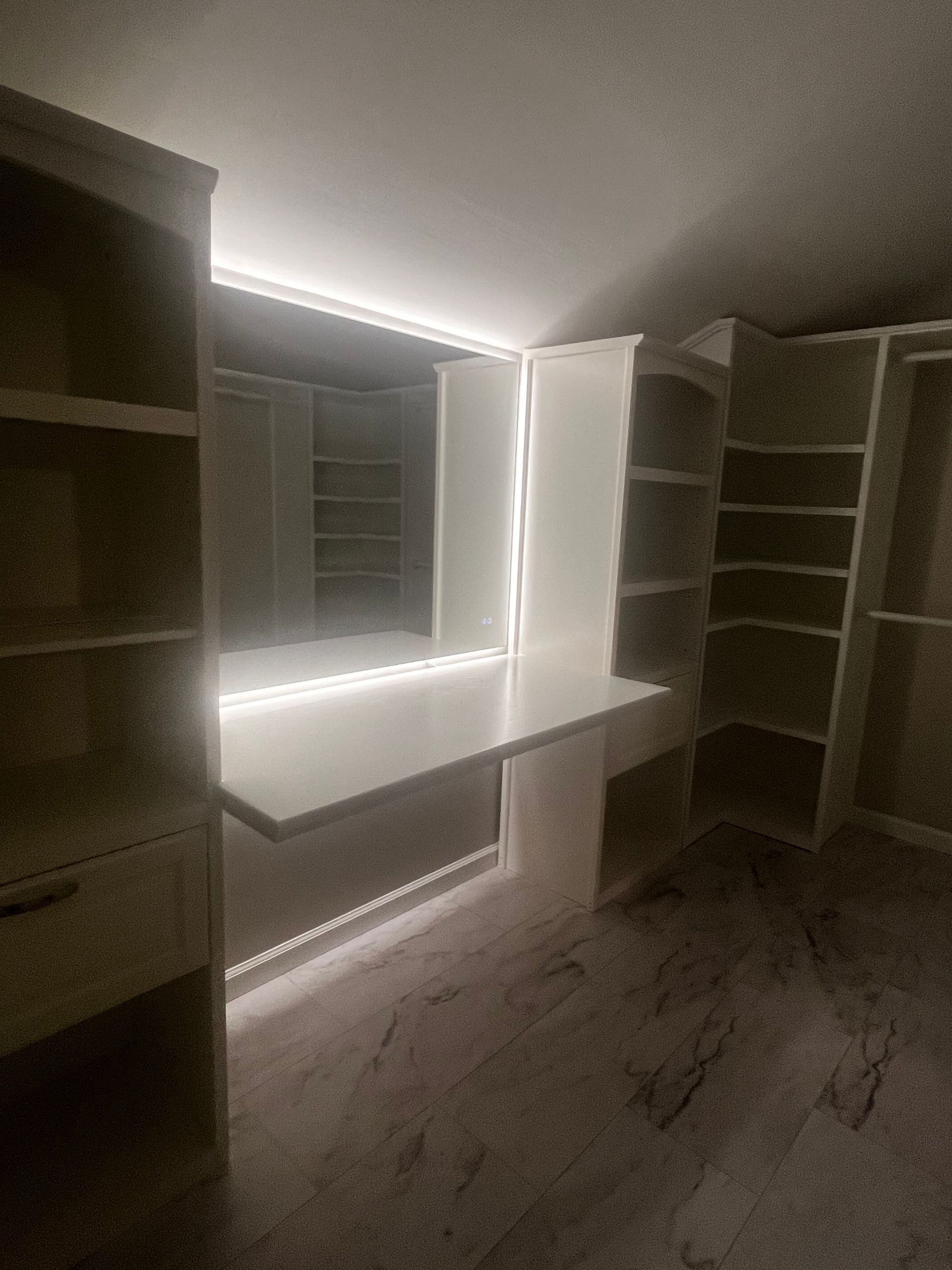 Dimly lit walk-in closet with built-in shelves and a backlit vanity mirror.